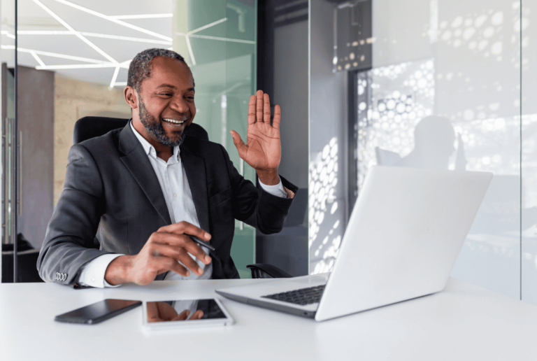 Man smiling and waving at computer screen, using tools for informal communication