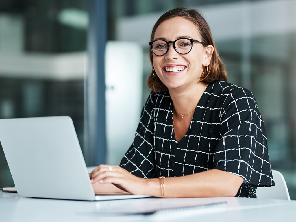 Female employee smiling typing on a laptop, showing team alignment through organized project execution and workflow clarity in office environment